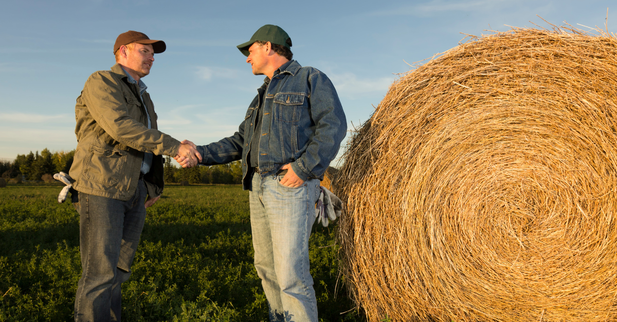 farmer shaking hands with lender beside a hay bales
